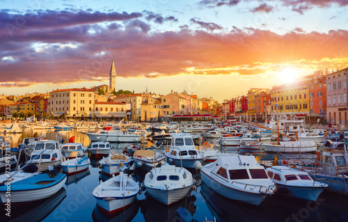Rovinj, Istria, Croatia. Motorboats and boats on water in port Rovigno. Medieval vintage houses of old town. Yachts landing, high tower Church Saint Euphemia. Morning sunrise sky withclouds