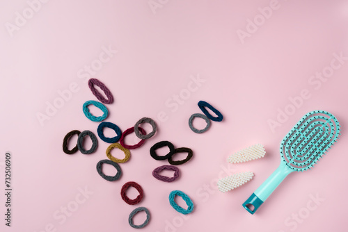 Blue hairbrush with lots of hair ties on a pink background.