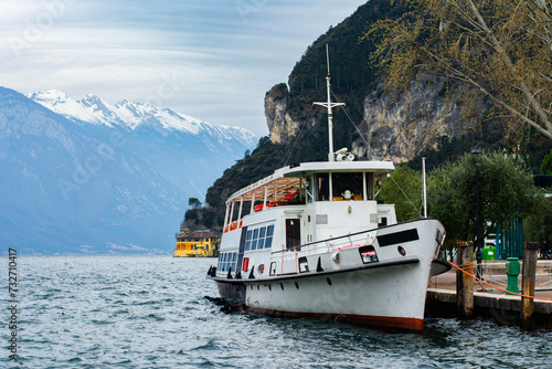 Waterfront view of the lake Garda with snowy mountains on the background and a boat in Riva del Garda, Trentino Alto Adige region, Italy.
