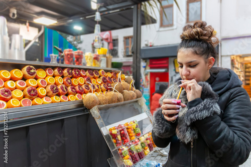 Young woman drinking healthy detox juice with straw. Female tourist enjoying takeaway freshly squeezed juice on the street. Healthy lifestyle concept
