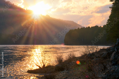 Evening Altai sunset landscape with river Katun and mountains with forest. The Sun sets behind the mountain and lights up the landscape with its last rays.