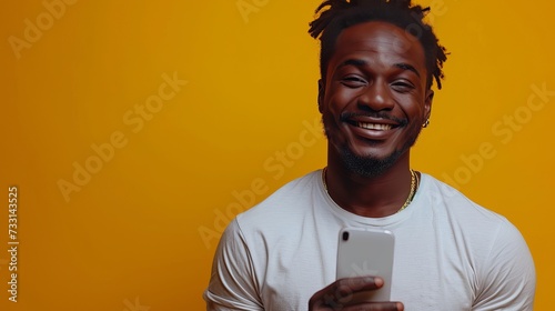 African American man posing on yellow studio background with a mobile phone screen recommending an app, smiling to camera.