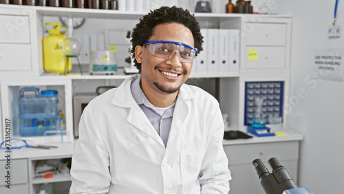 Smiling man wearing lab coat and safety goggles in scientific laboratory setting