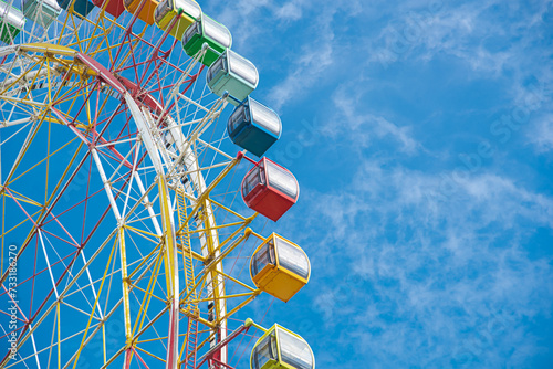 Colorful sightseeing cabin or multiple passengers carrying components with support frame, rim of modern Ferris Wheel at amusement park in Nha Trang, Vietnam, sunny blue cloud sky, spoke cable