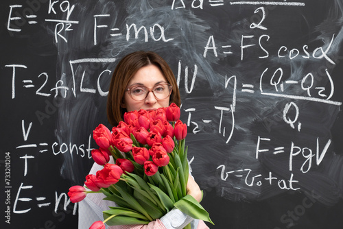 A young attractive teacher stands with a bouquet of flowers in the classroom. Teachers day and graduation concept