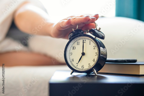 Person hitting snooze on a classic alarm clock