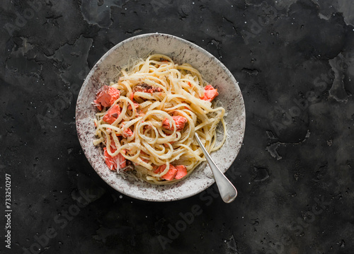 Bevette creamy pasta with baked trout on a dark background, top view