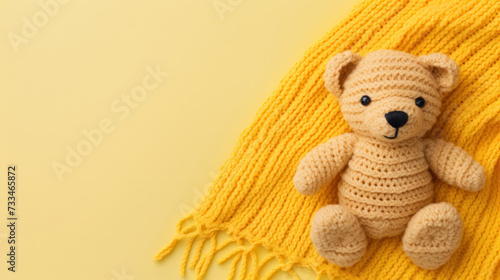 A small knitted amigurumi bear toy on a yellow blanket, on a yellow background. Flat lay, top view, copy space. space for text