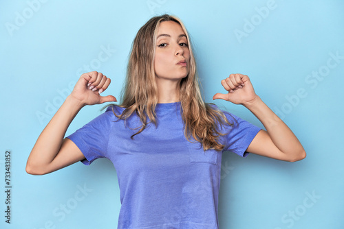 Blonde young caucasian woman in blue studio feels proud and self confident, example to follow.