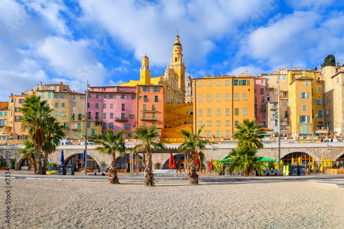 The colorful skyline including the Basilica Saint-Michael and steps to the old town above Plage des Sablettes beach and promenade in the colorful seaside town of Menton, France.