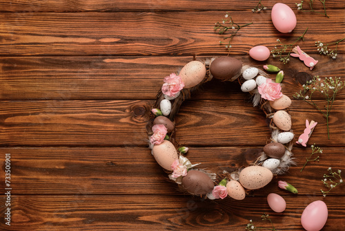 Easter wreath decorated with eggs and flowers on wooden background. Top view