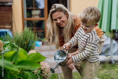 Mother and son taking care of plants in the garden, replanting, watering flowers. Mom and boy spending quality time together, bonding.