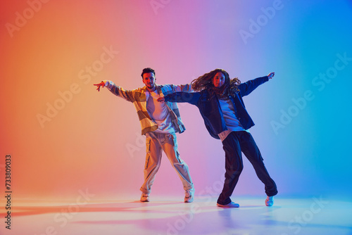 Dynamic photo of two fashion dressed people, dancing in motion against gradient studio background in neon light, filter. Concept of youth culture, music, lifestyle, style , action. Gel portrait.