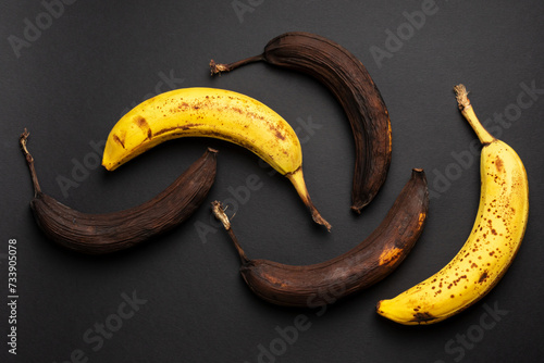 Rotten bananas on a black background from above. Bananas that are beginning to spoil and bananas that have already spoiled. Yellow and brown spoiled bananas.