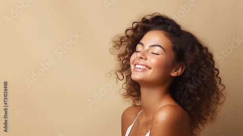 Portrait of smiling girl enjoying beauty treatment on beige background. Beautiful natural woman looking at copy space, spa and wellness concept. Carefree laughing woman with bare shoulders isolated.