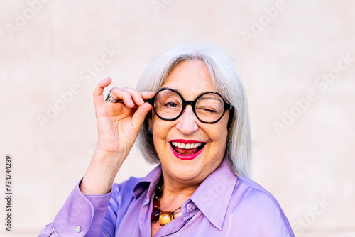 portrait of nice senior woman in glasses smiling and winking looking at camera, concept of elderly people happiness and active lifestyle, copy space for text