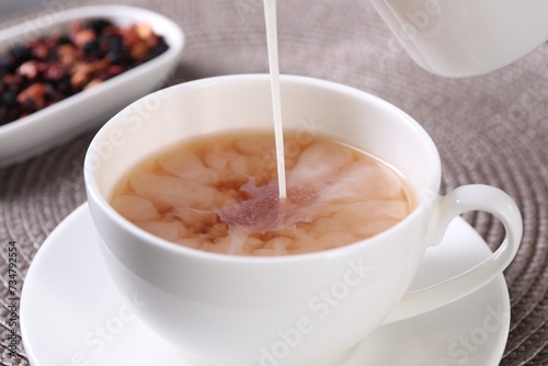 Pouring milk into cup with aromatic tea at table, closeup