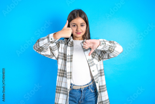 Young beautiful teen girl wearing check shirt showing thumbs up and thumbs down, difficult choose concept