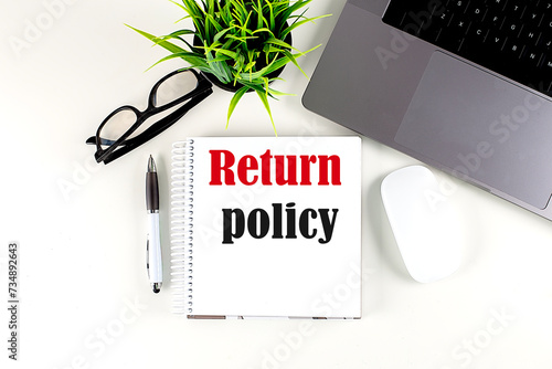 RETURN POLICY text written on notebook with laptop , pen, glasses and mouse , white background