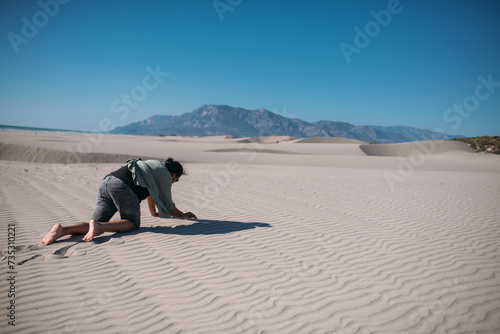 An emaciated man crawls under the scorching sun on the sand in the desert.