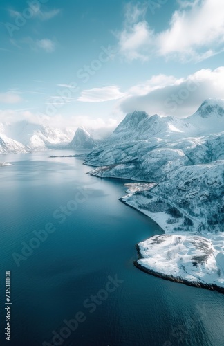 an aerial view of a large body of water surrounded by snow covered mountains and a blue sky with white clouds.