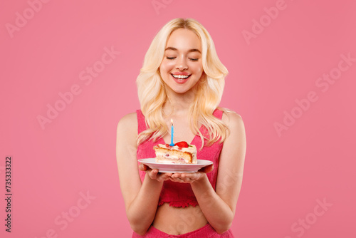 Blissful young woman with birthday cake, eyes closed in wish
