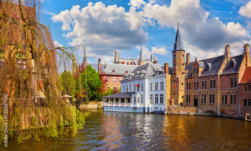 Bruges, Belgium. Ancient medieval european city. View at tower and vintage building on the banks of Rozenhoedkaai channel river. Panoramic view with blue sky clouds. Famous tourist attraction.