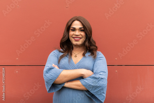 Portrait of happy trans woman with crossed-arms. Blue dress, red background. LGBT concept.