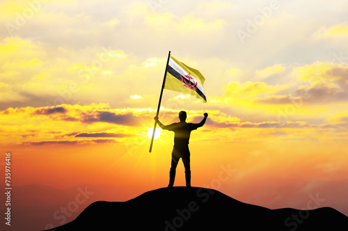 Brunei flag being waved by a man celebrating success at the top of a mountain against sunset or sunrise. Brunei flag for Independence Day.