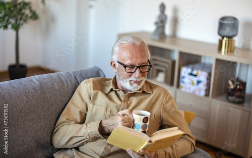 Close up of old happy and relaxed man sitting reading a book at home. Mature male person enjoying free time having fun indoor.