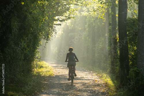 femme cycliste de dos sur un chemin en foret, vue horizontale, lumière d'été