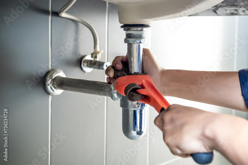 Plumber uses wrench to repair water pipe under sink There is maintenance to fix the water leak in the bathroom.with red wrench, plumbing install concept.