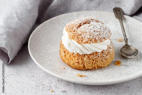 Cream puffs, semla, pastry from choux covered sugar powder on white plate over stone table background. Sweet dessert with chantilly cream