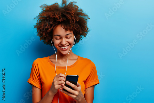 Young african american woman listening to music with earphones and mobile phone on blue background 