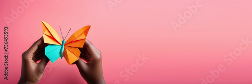 horizontal banner, Zero Discrimination Day, multicolored paper butterflies, rainbow coloring, origami butterfly in the hands of an African American woman, pink background, place for text