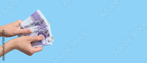 Female hands holding pound sterling banknotes on light blue background with space for text