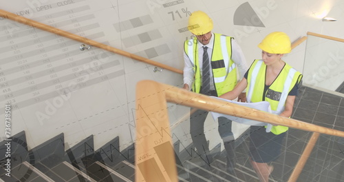 Digital composite of male and female Caucasian architects walking up the the stairs wearing safety c