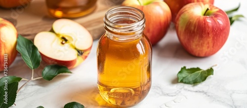 A bottle of apple cider vinegar, a food ingredient, sits on a table beside fresh apples. The liquid drinkware is a natural plantbased fluid used in recipes