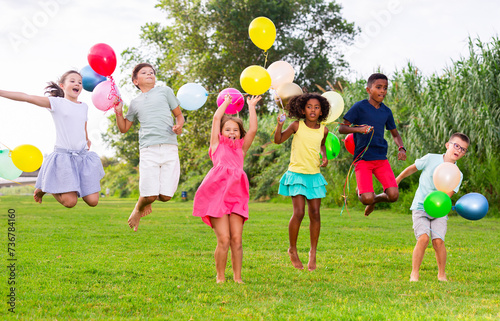 Barefoot children jumping on field with balloons in hands and smiling.