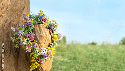 colorful flowers wreath on tree on meadow. summer background. Floral crown, symbol of Summer Solstice Day, Midsummer holiday, Litha sabbat. witch, wiccan ritual. copy space