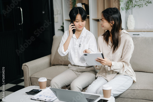 Two Asian businesswoman discuss investment project working and planning strategy with tablet laptop computer on sofa