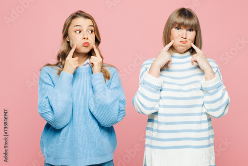 Elder cheerful parent mom 50s years old with young adult daughter two women together wear blue casual clothes point on puffed cheeks isolated on plain pastel light pink background. Family day concept.