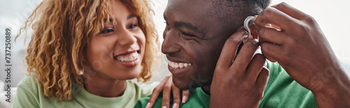 deaf and happy african american man wearing hearing aid near girlfriend, health device banner