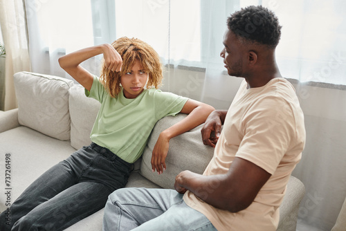 african american woman gesturing while looking at boyfriend on sofa, nonverbal communication