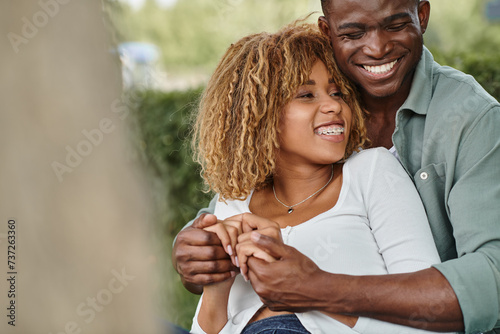 excited african american couple spending quality time with each other in park, holding hands