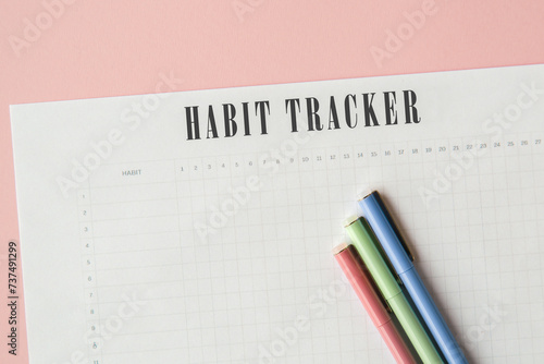 sheet of paper with habit tracker and multi-colored pens on a pink background, concept of motivation and self-improvement