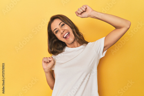 Middle-aged caucasian woman on yellow celebrating a special day, jumps and raise arms with energy.