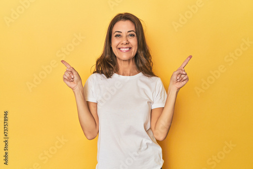 Middle-aged caucasian woman on yellow pointing to different copy spaces, choosing one of them, showing with finger.