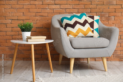 Grey armchair with cushion and coffee table near brown brick wall