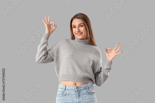 Young woman showing OK on light background